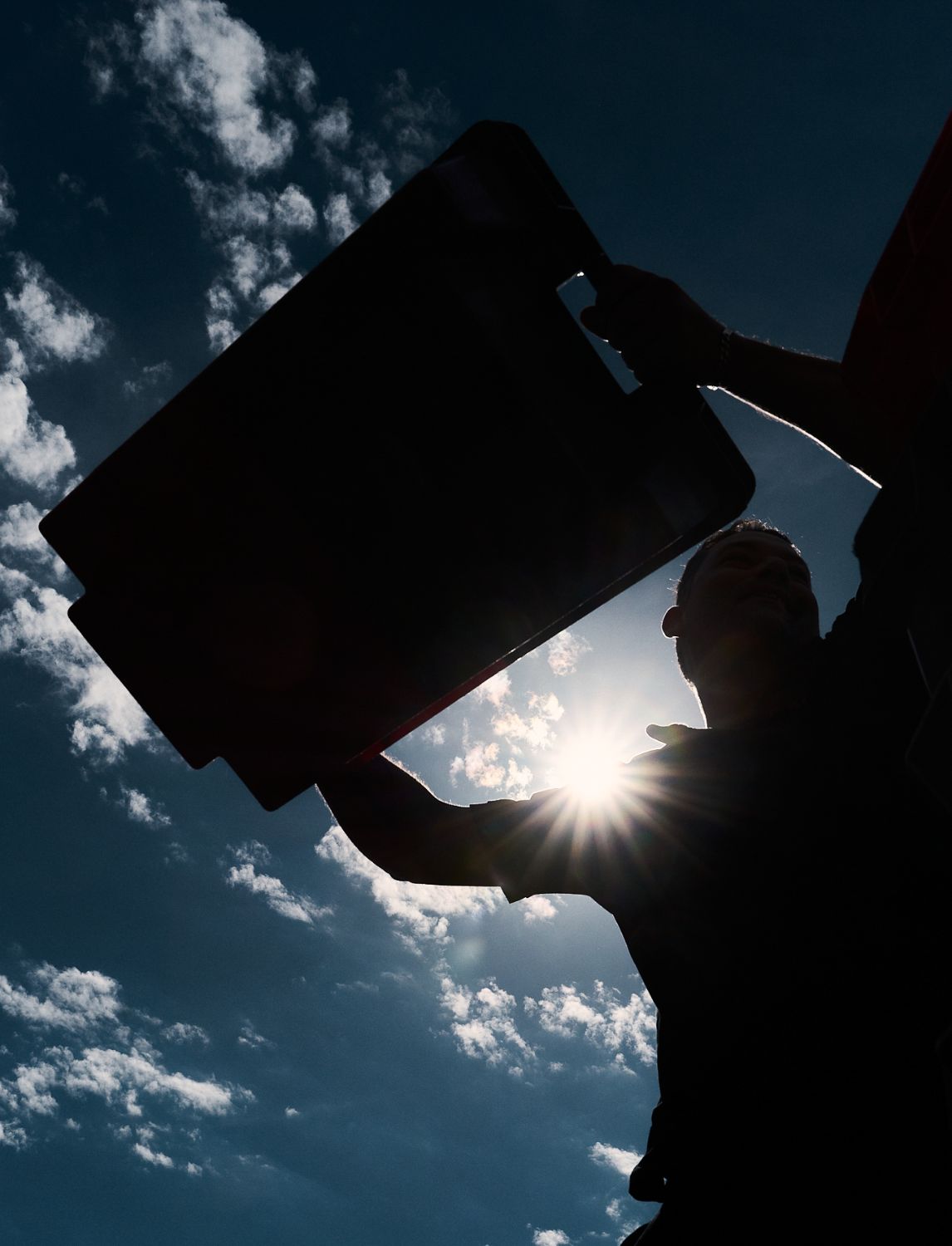 A man seen from below lifting a harvest crate up against a clear blue sky.