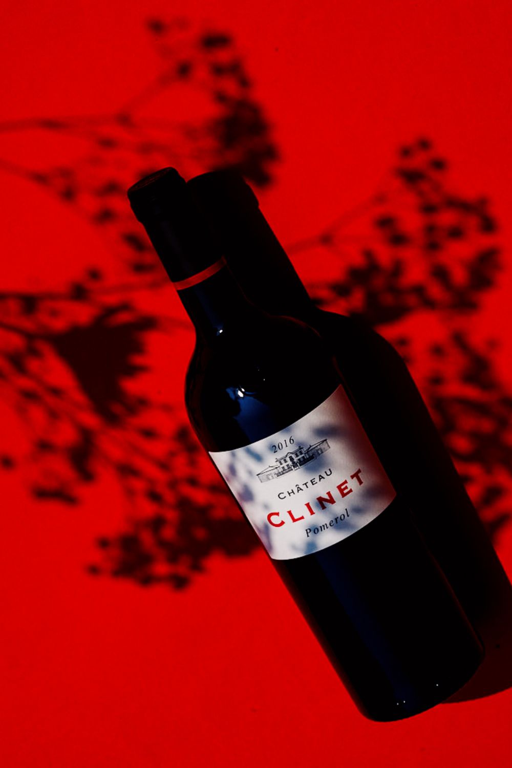 Clinet bottle on a red background, shadows of country flowers playing with the bottle.