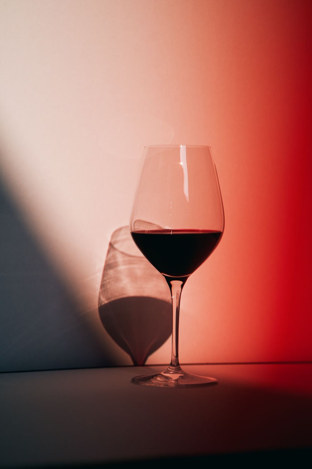 A glass of red wine lit by red light and projecting shadow onto a white background.