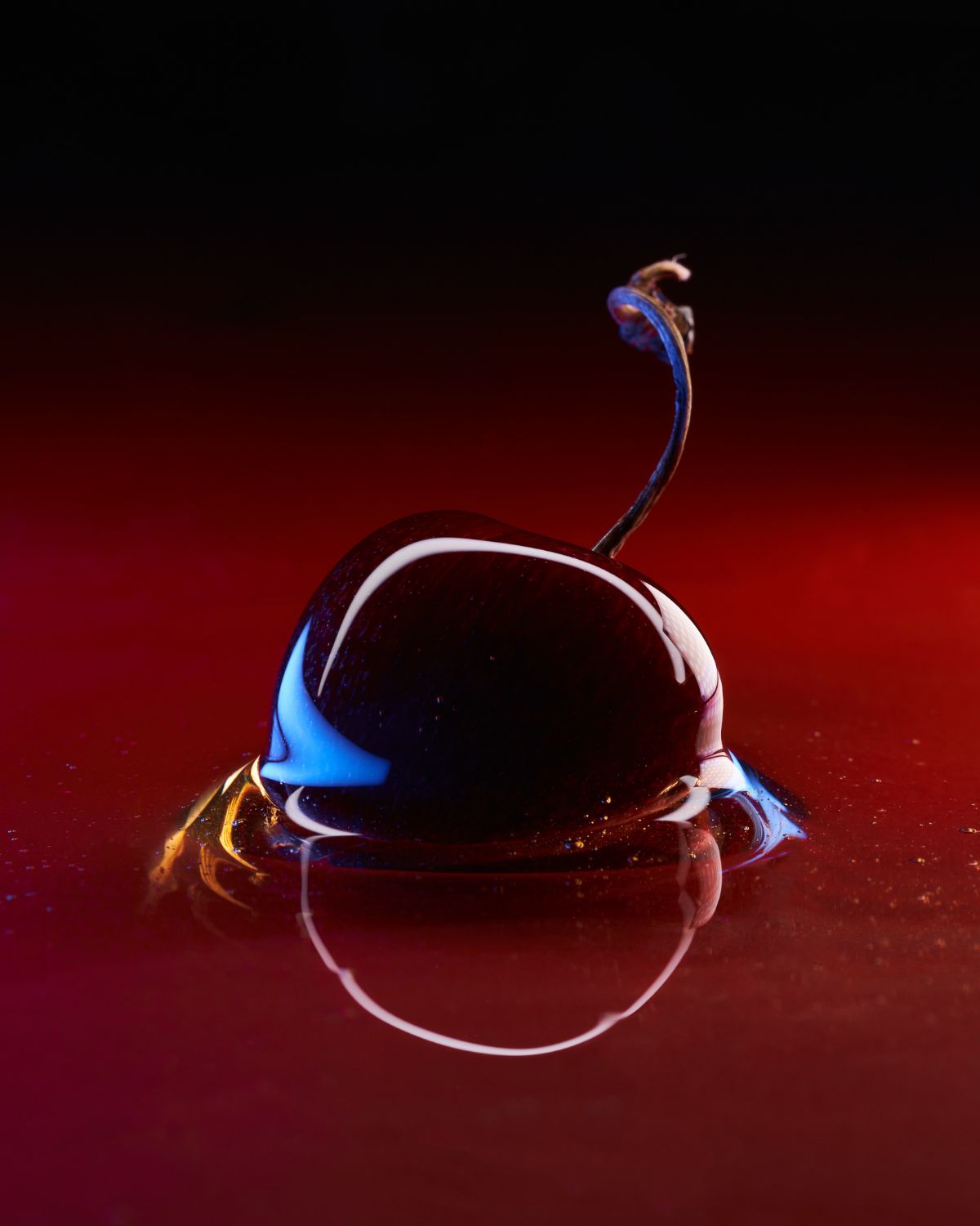 Cherry in shiny liquid texture, mirror effect on a red background.