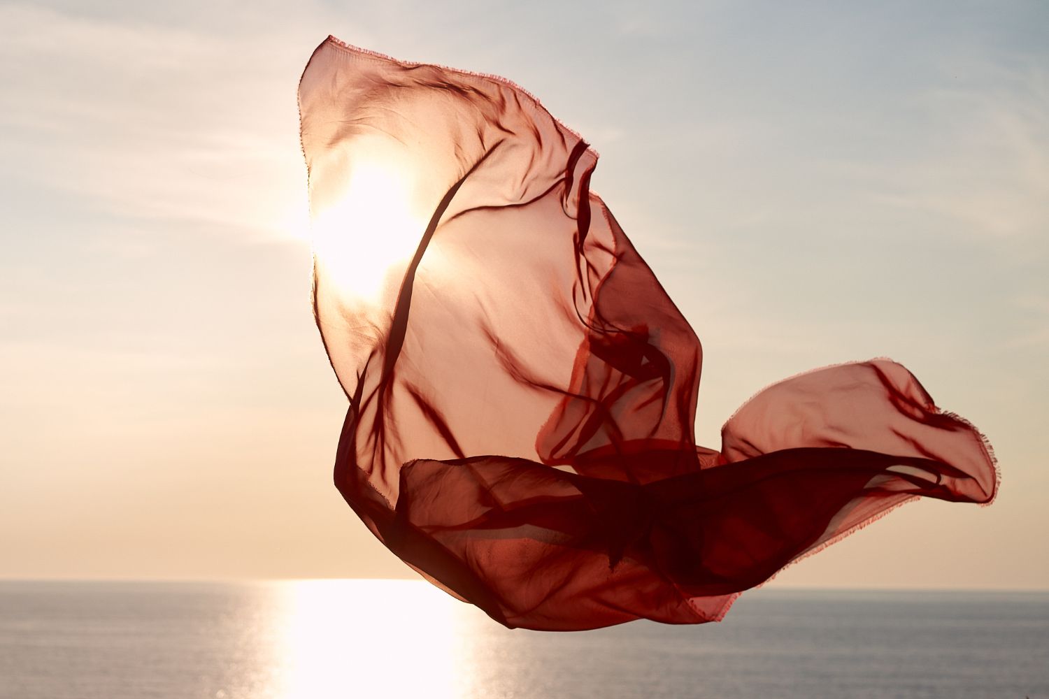 Lanscape of red fabric flying in the sun with sea in background.