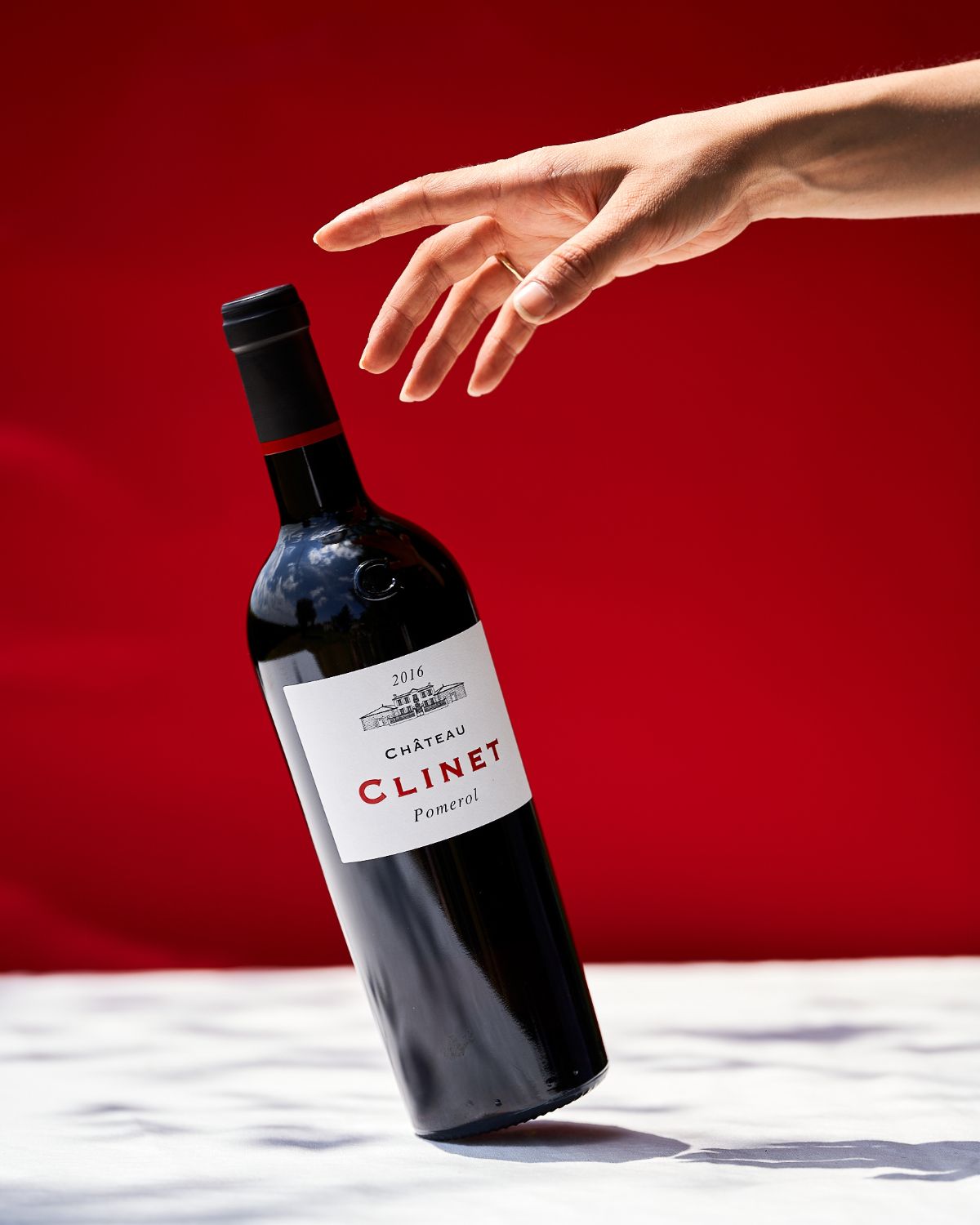 A hand reaching out to a bottle of Clinet, leaning over against a white and red background.